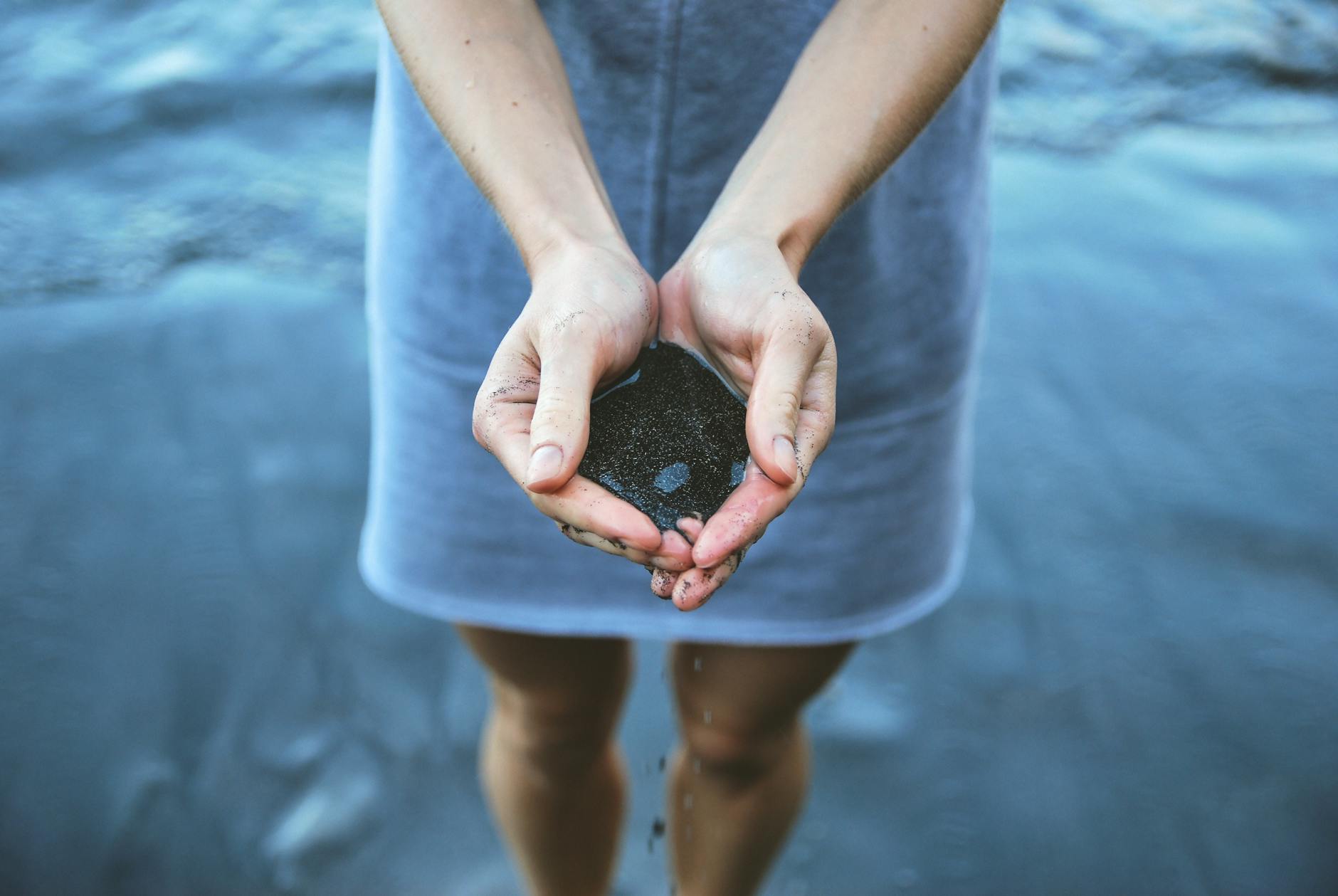 woman holding black sand on seashore du